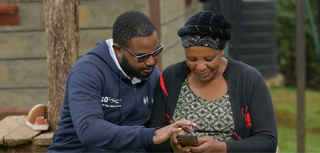 Kenyansk yngre man visar kenyansk äldre kvinna hur man använder en smartphone