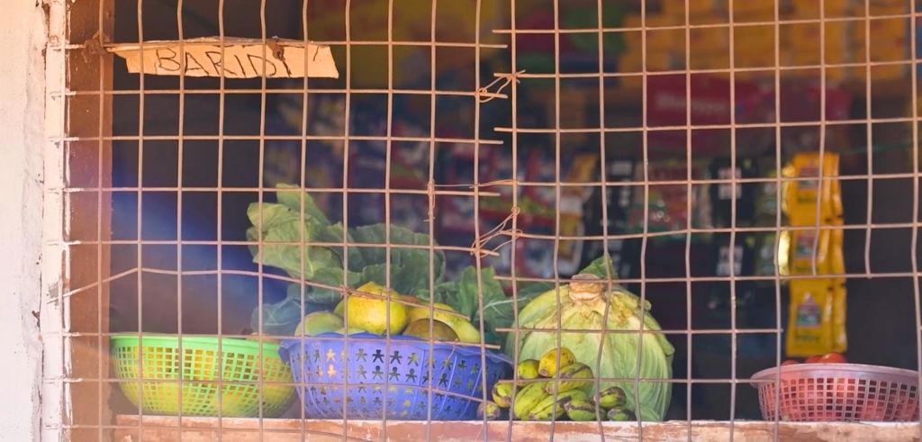 Färska grönsaker och frukter bakom ett gallerfönster i en liten butik, med en skylt som säger "BARIDI" ovanför.