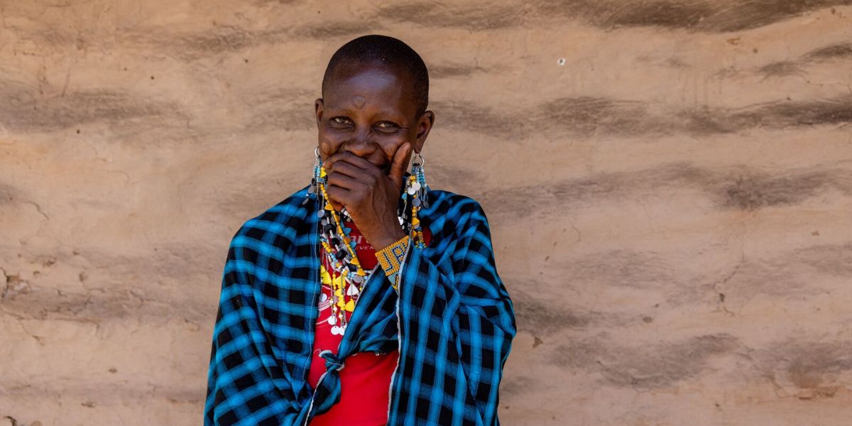 Kvinna i Tanzania skrattar bakom handen framför lerklinad vägg.